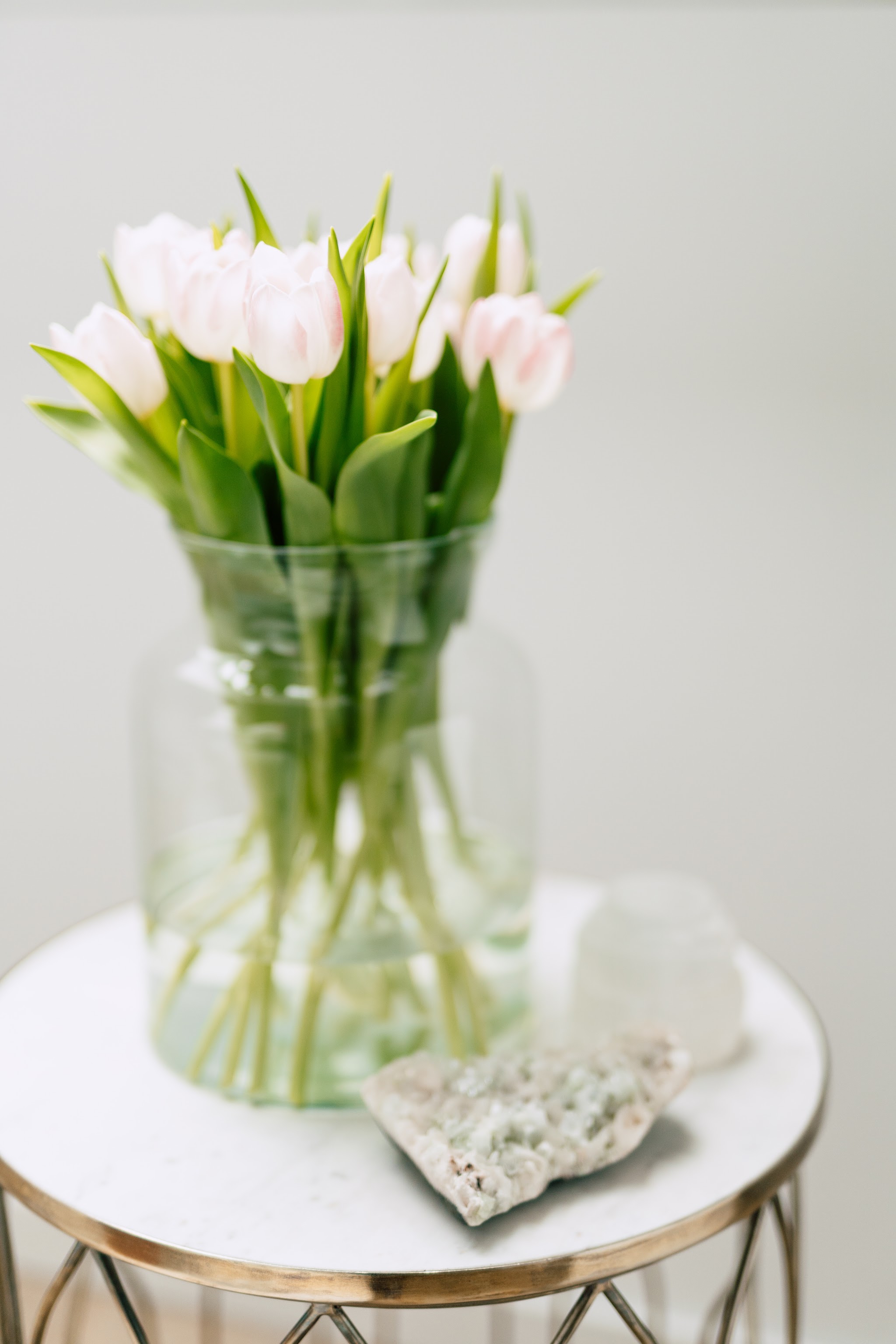 Witte tulpen in een glazen vaas op een gouden bijzettafel